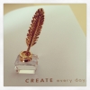 calissa: Photo of Swarovski crystal & gold figurine of inkpot and quill sitting on a page that says 'create every day' (Writing)